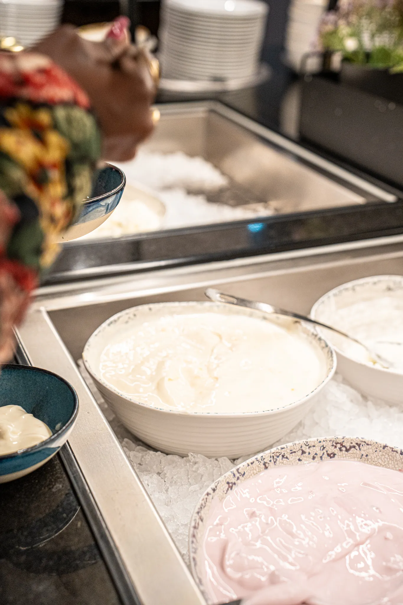 Mehrere Schalen mit weißem und rosafarbenem Joghurt stehen in einem gekühlten Buffet mit Eis.