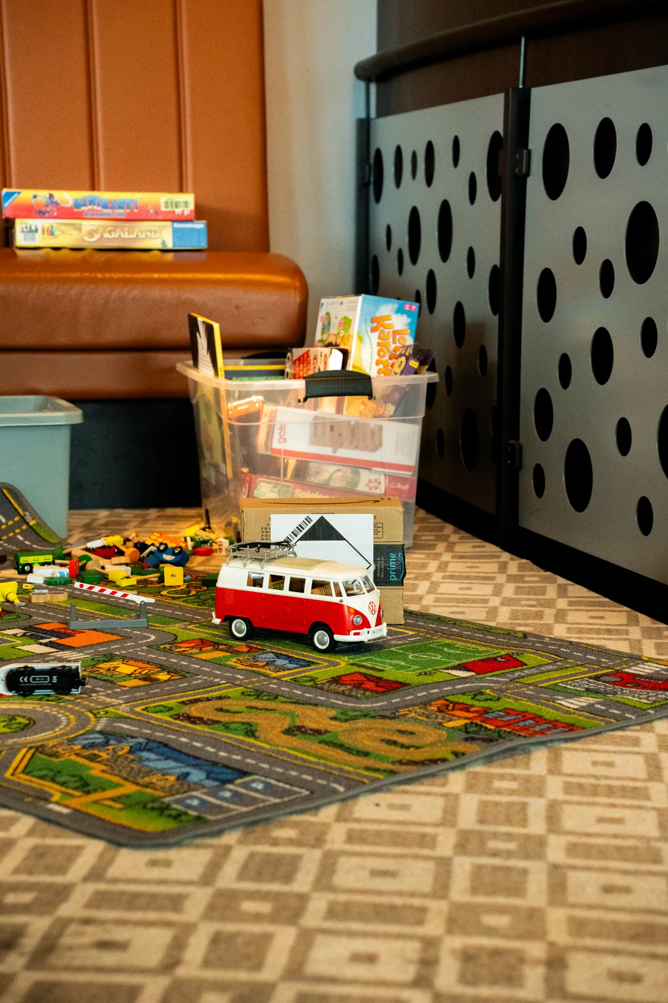 Spielteppich mit Straßenmotiven, darauf ein rotes Spielzeugauto, daneben eine Kiste mit Kinderbüchern und Bastelsachen.
