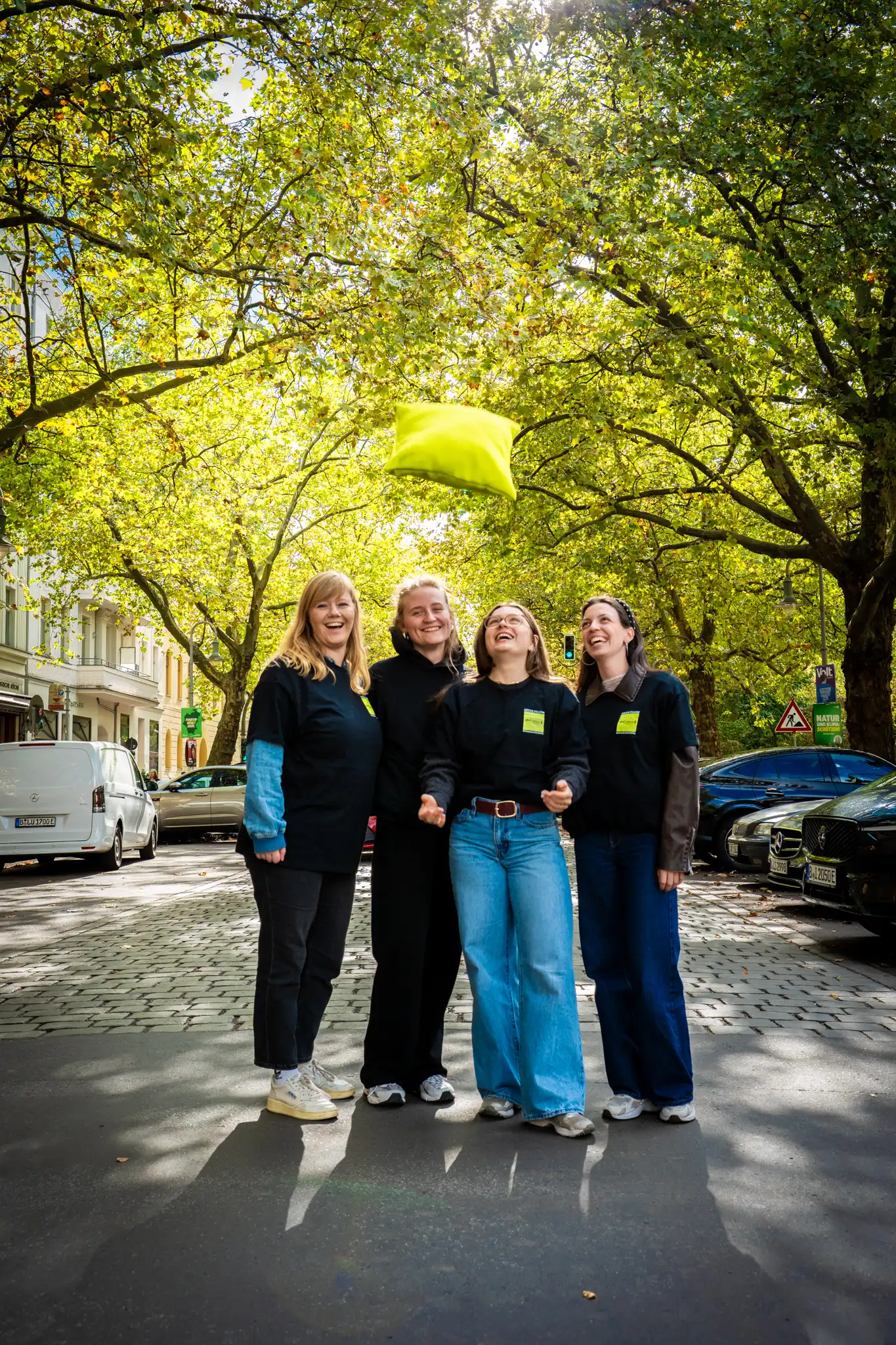 Four people stand on a tree-lined street; a green object floats above them.