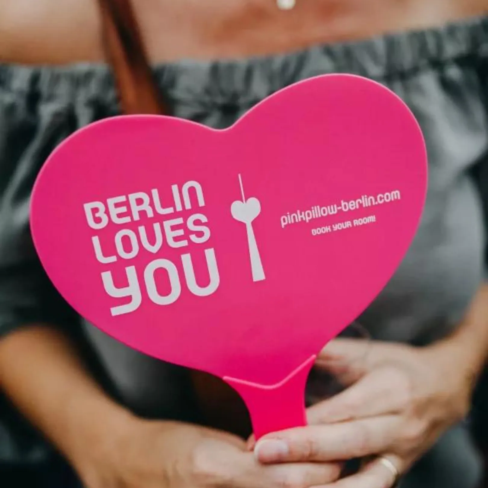 A person holds a pink heart sign with the text "BERLIN LOVES YOU" and a stylised fork in their hands.