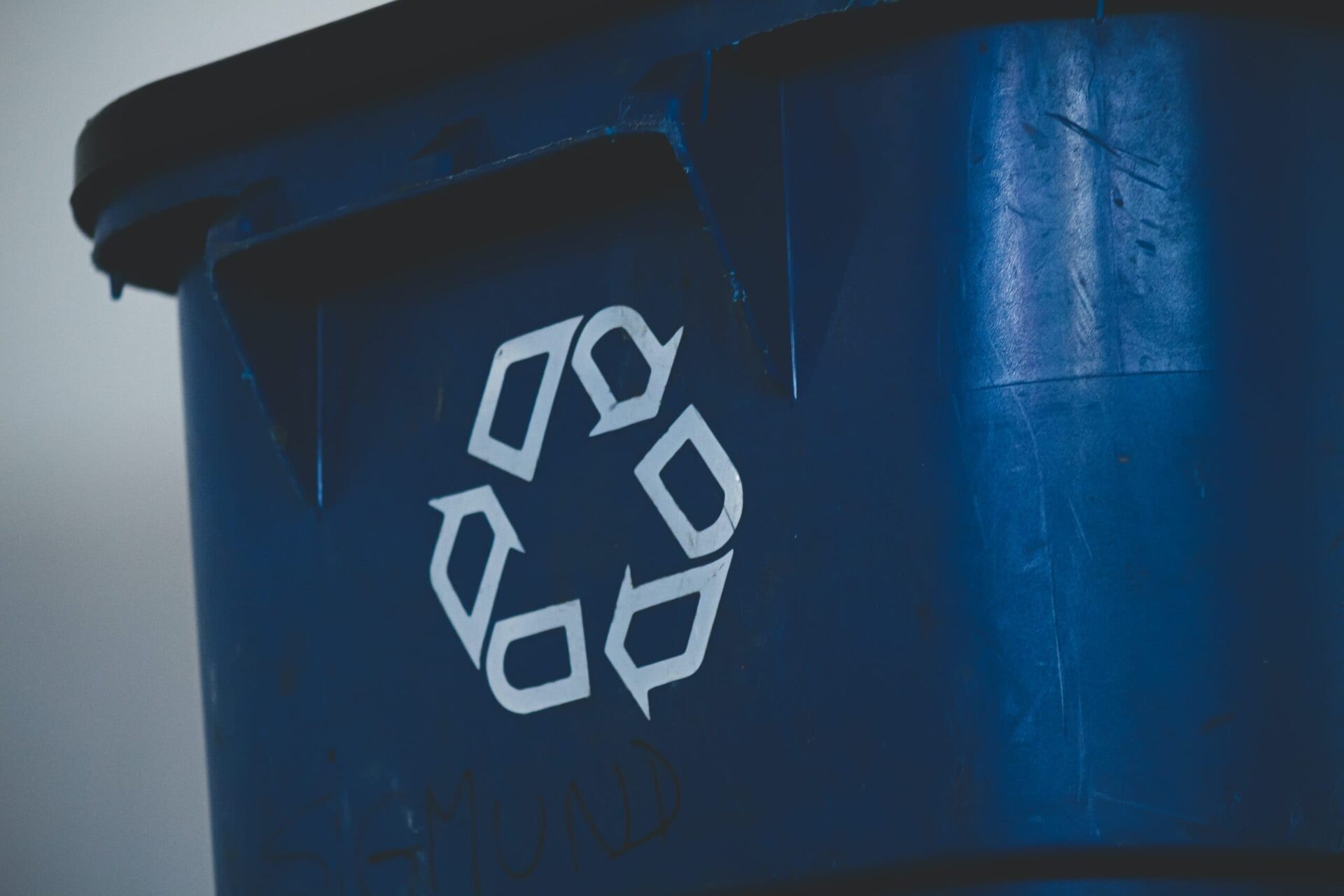 Close-up of a blue waste container with a white recycling symbol on the front.