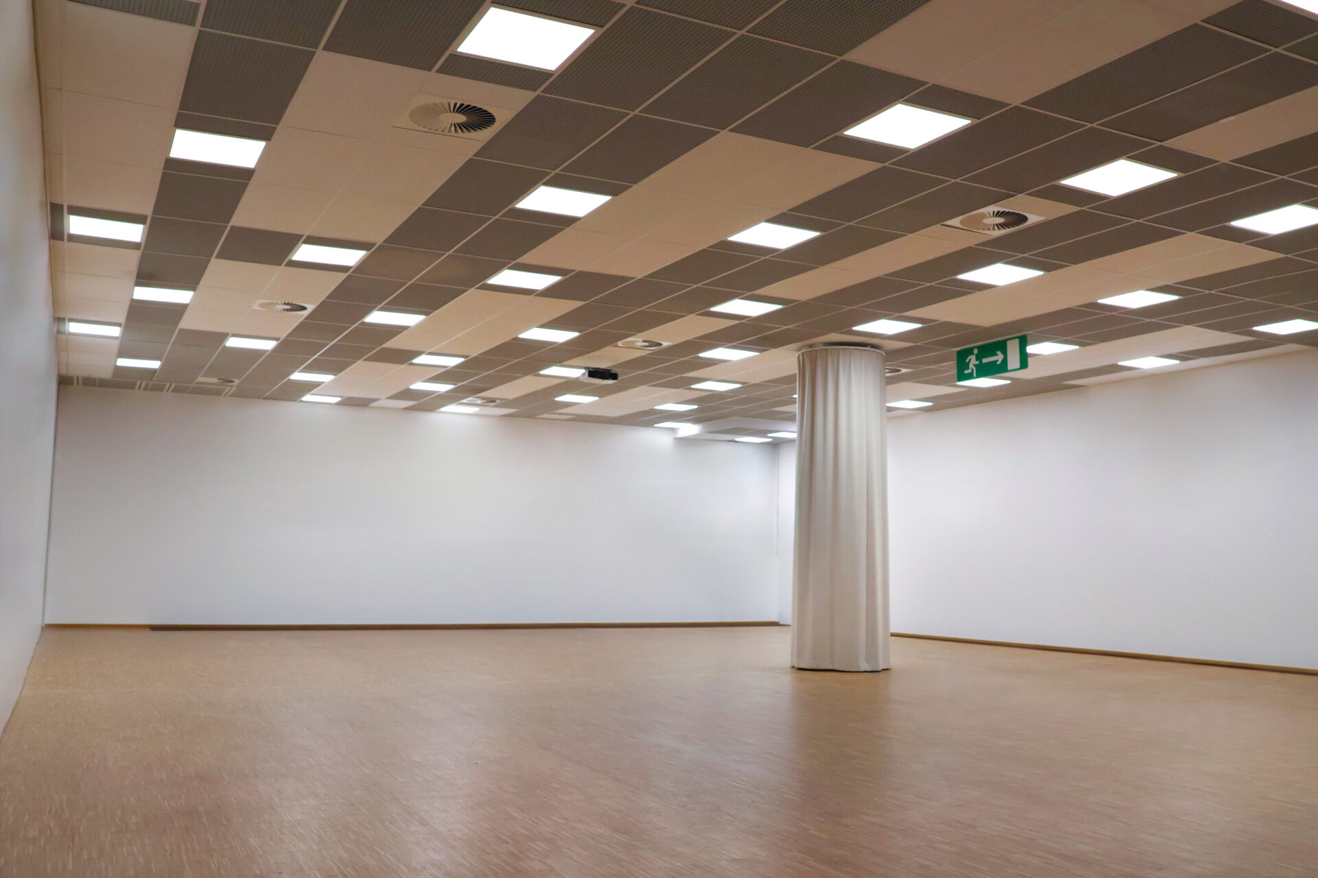 Ein großer, leerer Veranstaltungsraum mit einer hellen Deckenbeleuchtung, Säulen, einem Holzfußboden und flexiblen Trennwänden.