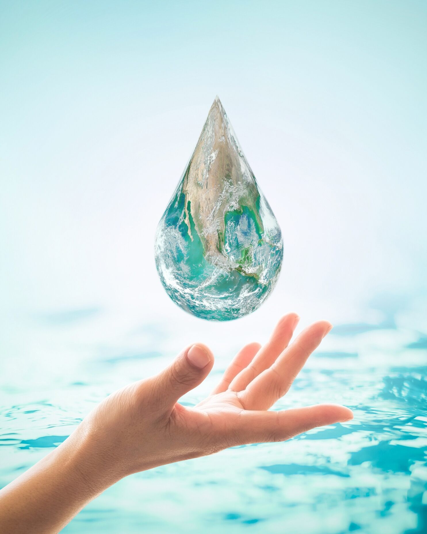 Eine Hand schwebt unter einem tropfenförmigen Objekt mit türkisfarbenen und sandfarbenen Strukturen vor einer hellen Wasseroberfläche.