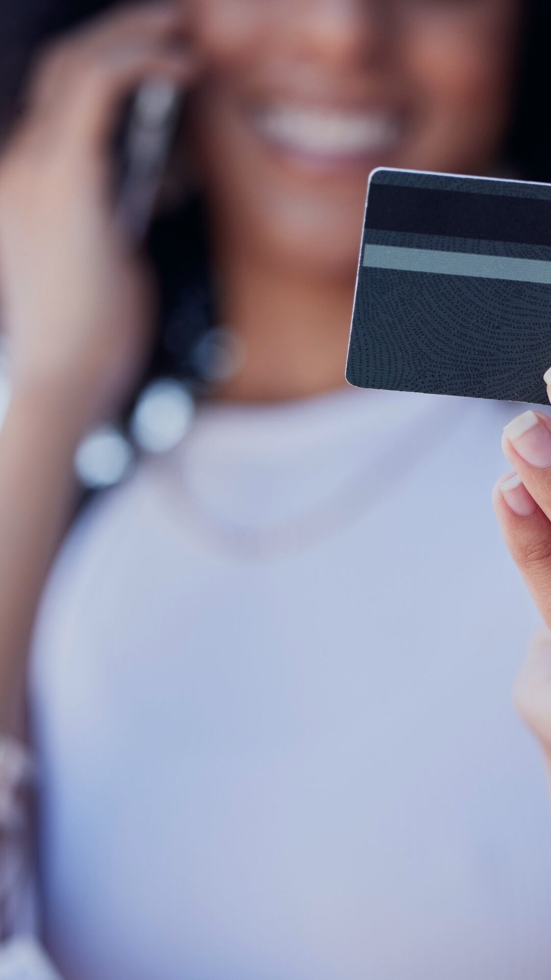 A person holds a dark payment card in their hand while talking on a phone.
