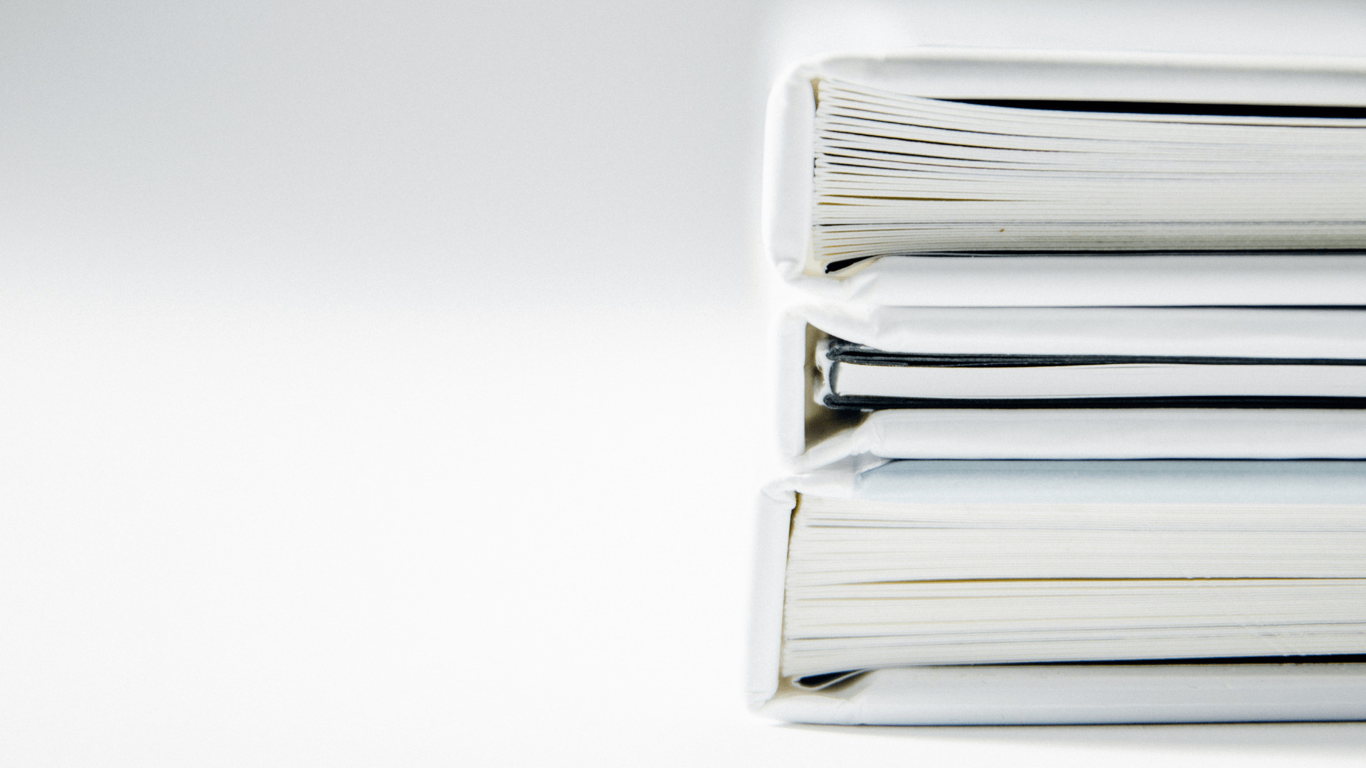 Two thick stacks of white books lying horizontally on top of each other, pages slightly fanned out.