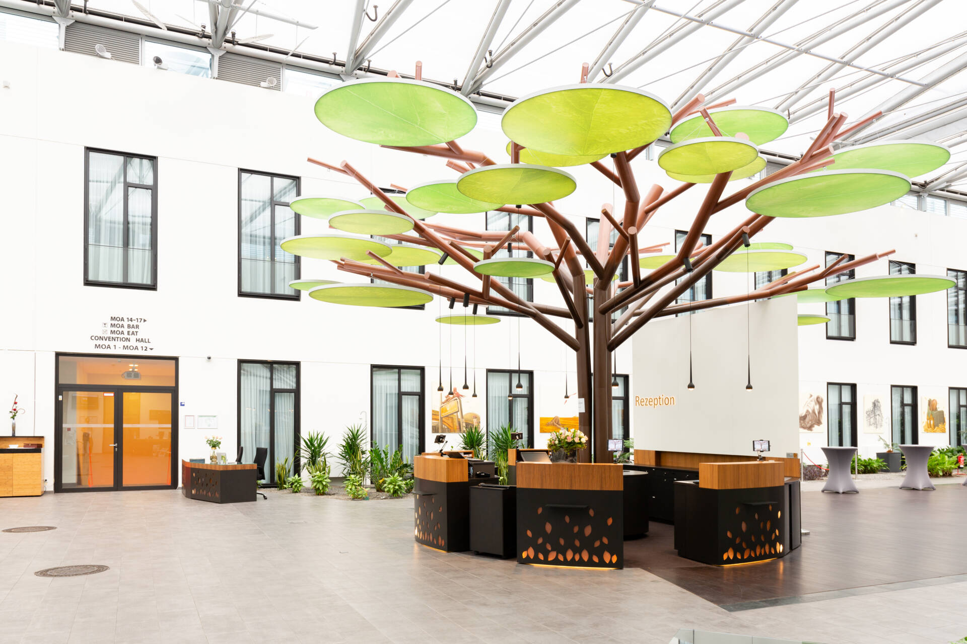 An open reception area in a Berlin coworking space with a modern, tree-shaped counter and green, round ceiling panels.