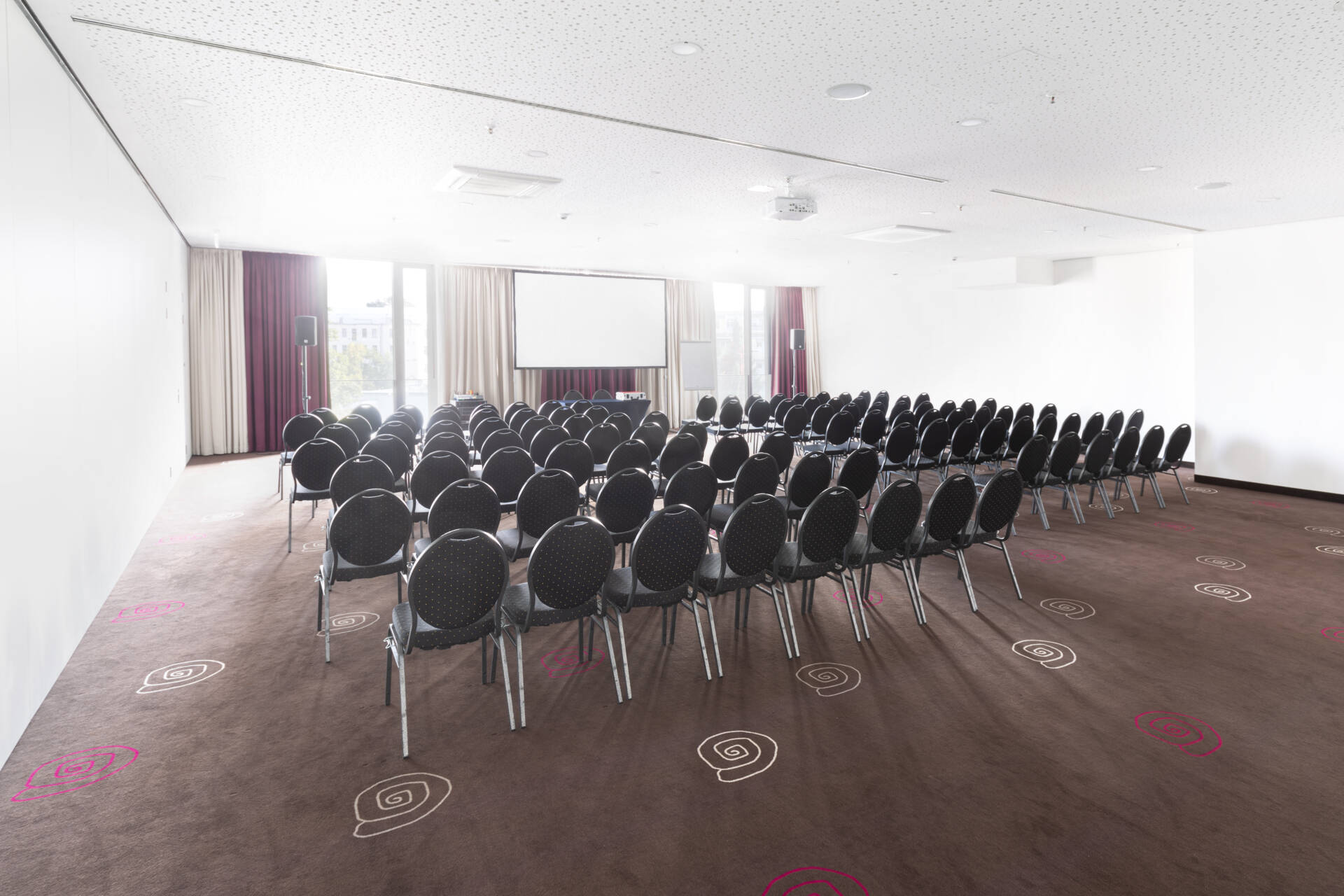 Ein professioneller Veranstaltungsraum mit einer Reihenbestuhlung, Bühne, Leinwand und Lichttechnik für Konferenzen und Events.