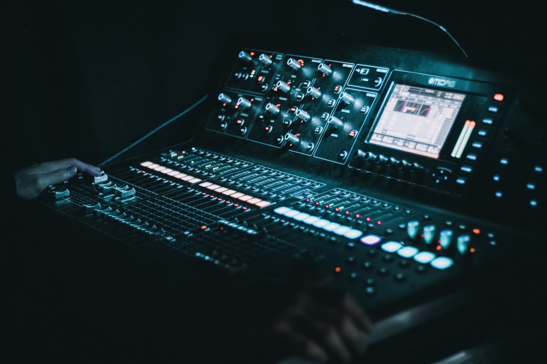 A mixing console with illuminated faders and a display with two hands on it, in a dark setting in a fully equipped event venue in Berlin Mitte.