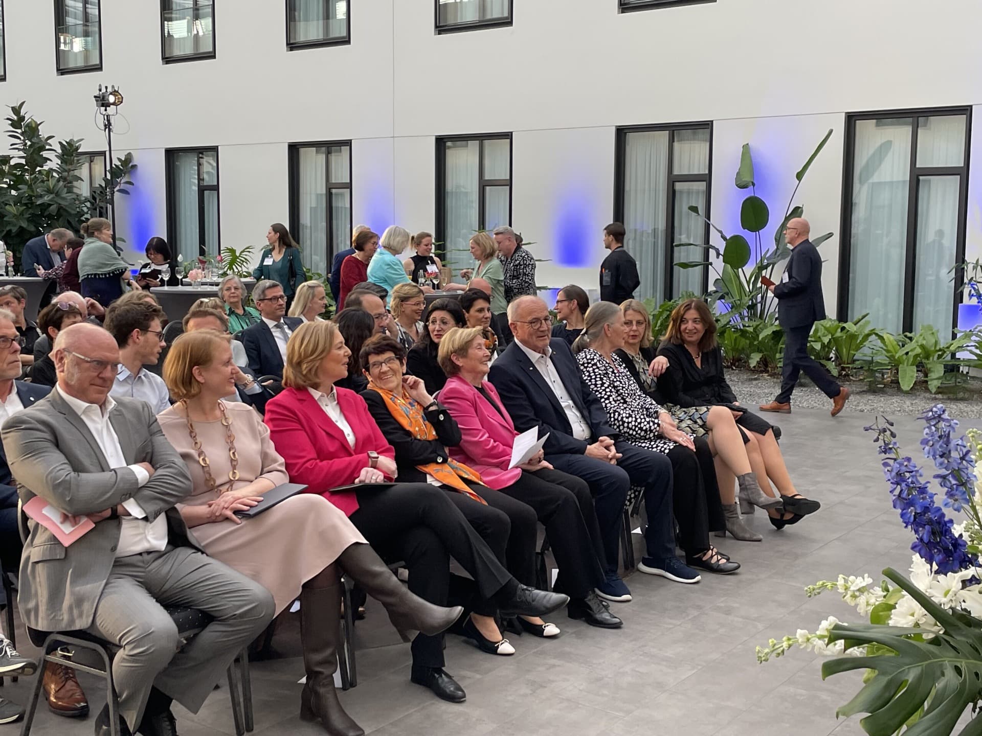 Several people sit in a row on chairs in an atrium with white walls and blue lighting accents at Hotel MOA Berlin.