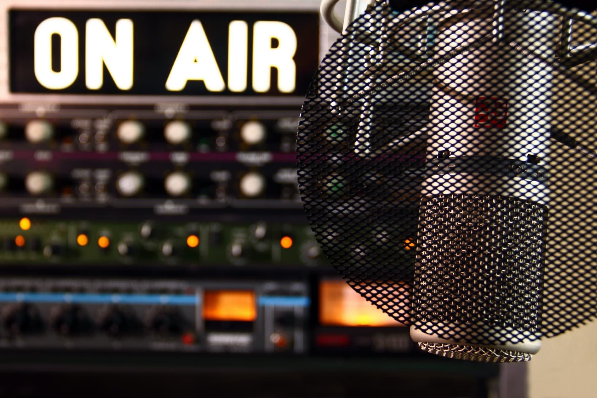 A close-up of a microphone head with a pop filter in front of a mixing console and a glowing "ON AIR" sign at the MOA event venue in Berlin Mitte.