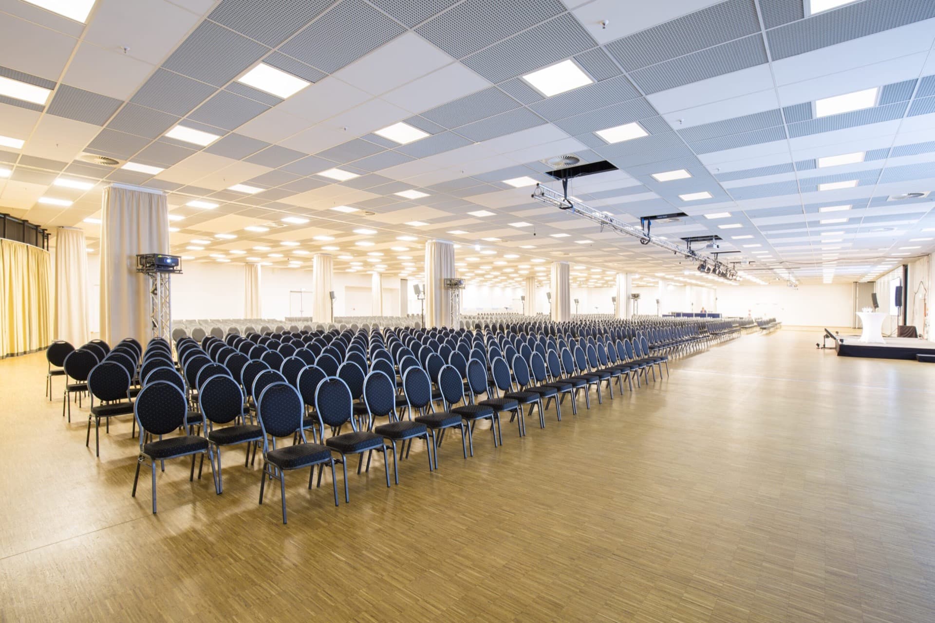 Ein großer heller Konferenzraum mit Reihen von schwarzen Stühlen und Holzfußboden in einer Eventlocation im Hotel MOA Berlin in Moabit.