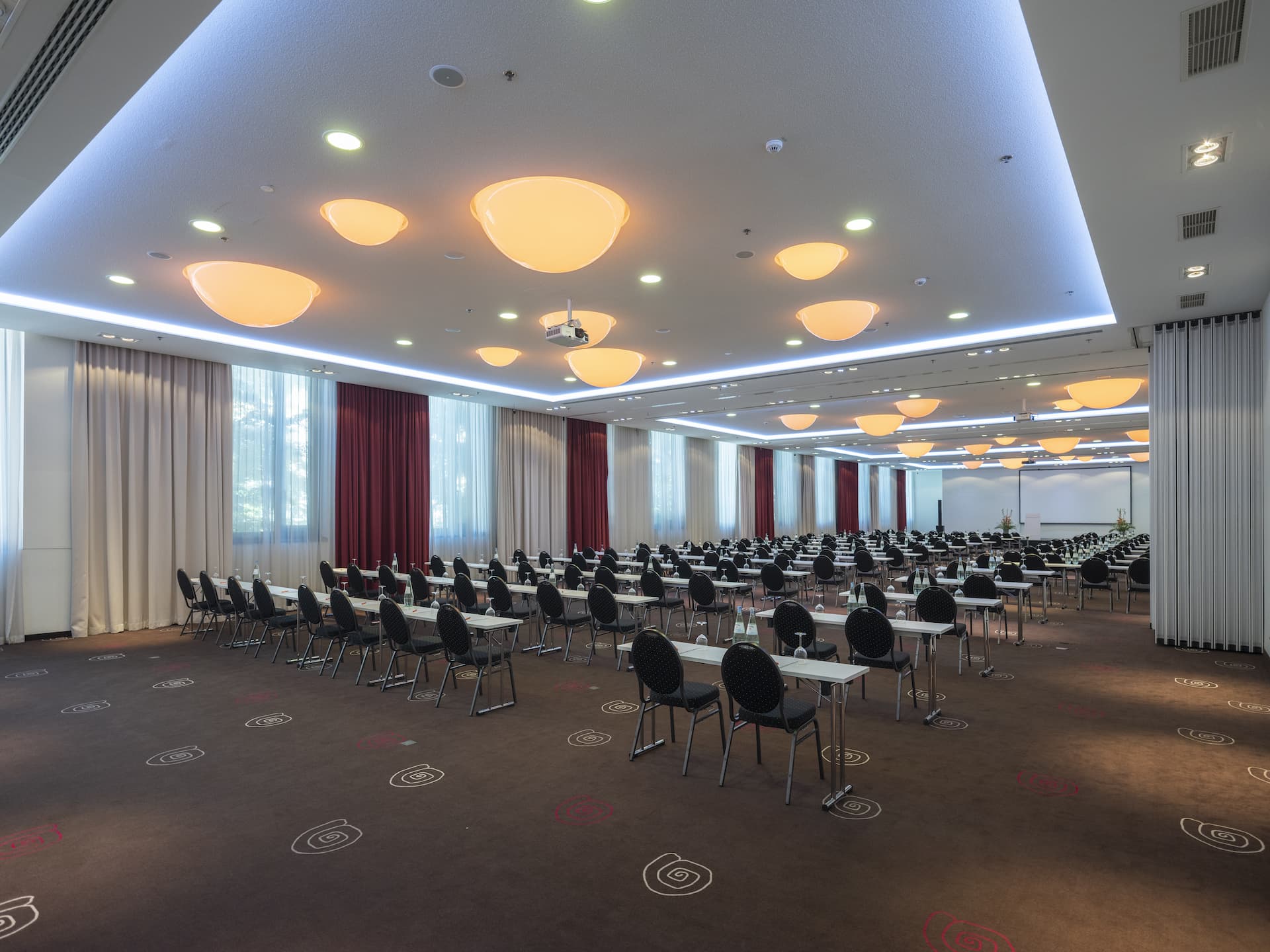 Ein heller Seminarraum mit einer parlamentarischen Reihenbestuhlung, Tischen, Stühlen und einer Leinwand.