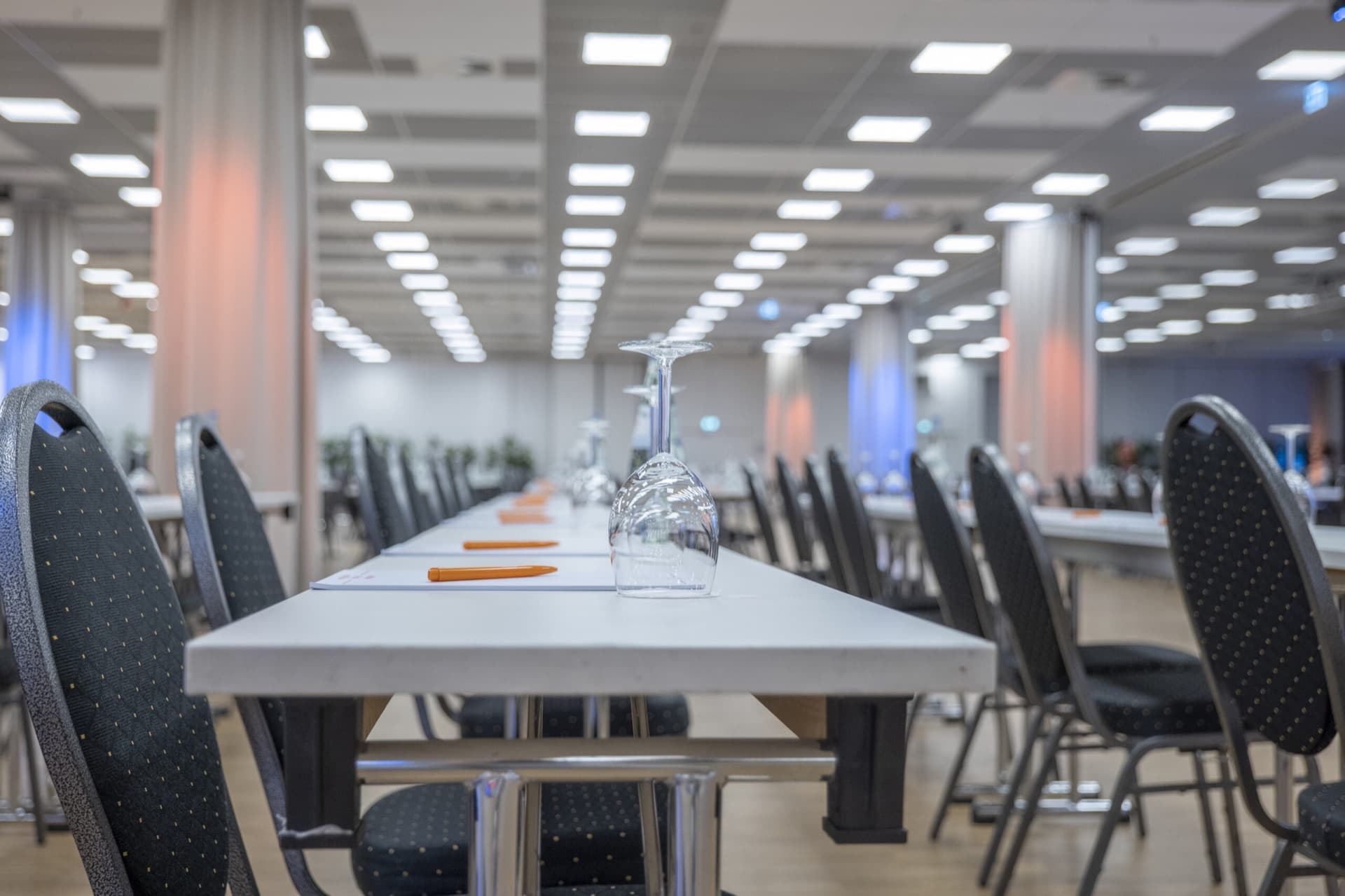 Ein langer Konferenztisch mit aufgestellten Weingläsern und Stühlen in einem großen, hell beleuchteten Tagungs- und Konferenzraum in Berlin Mitte.