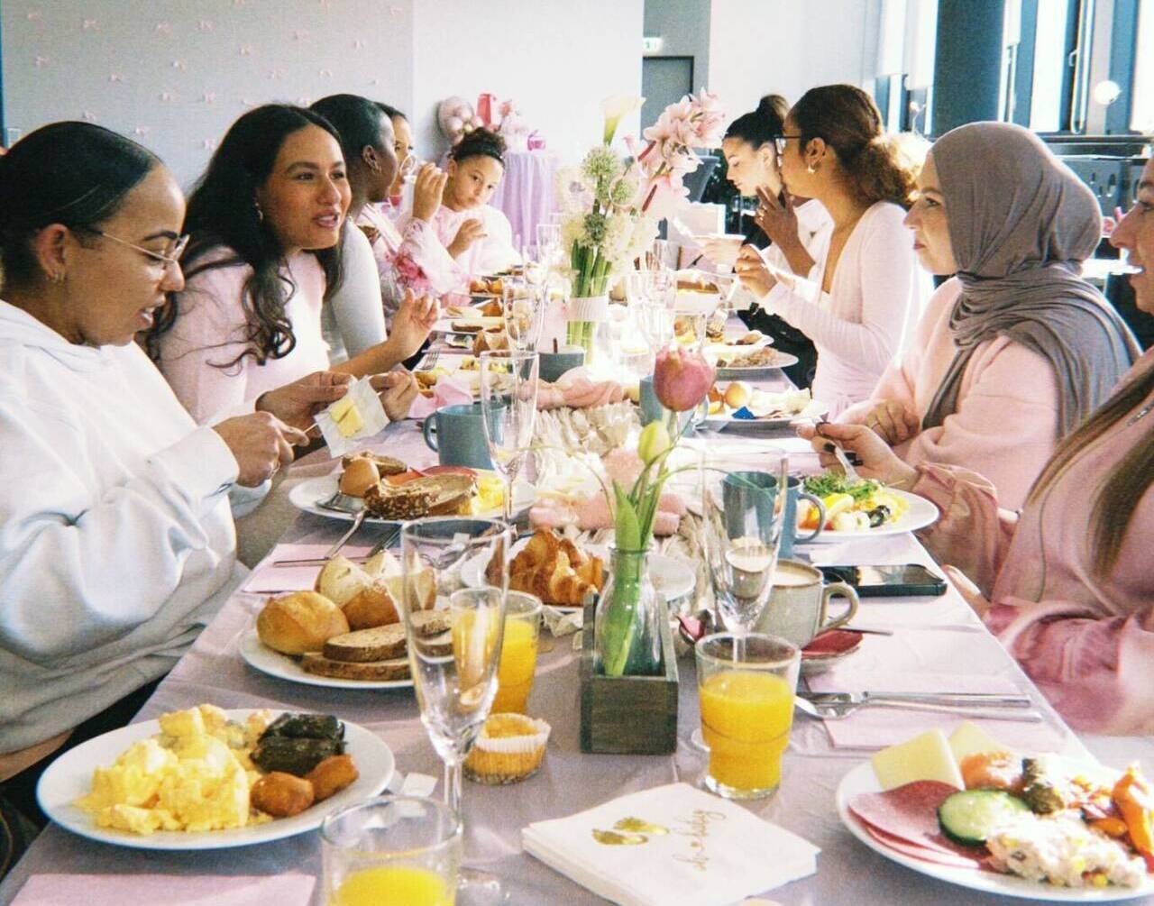 Eine Gruppe von Frauen sitzt an einer festlich gedeckten Tafel und isst gemeinsam in einem hellen Raum.