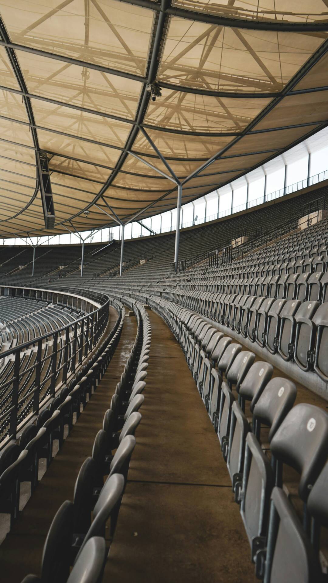 Curved stands with numerous grey seats and a covered roof in a vast stadium.