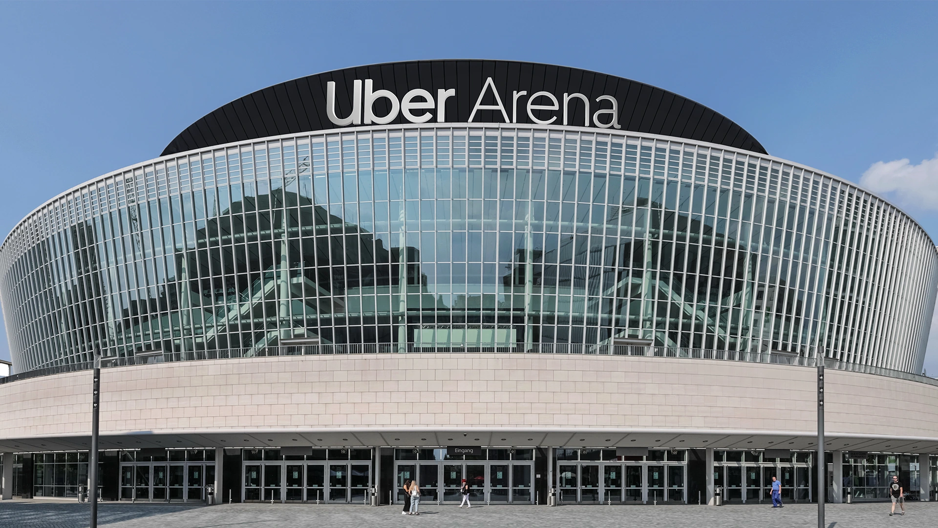 The exterior view of the Uber Arena with its curved glass facade, numerous entrances and the lettering „Uber Arena“.