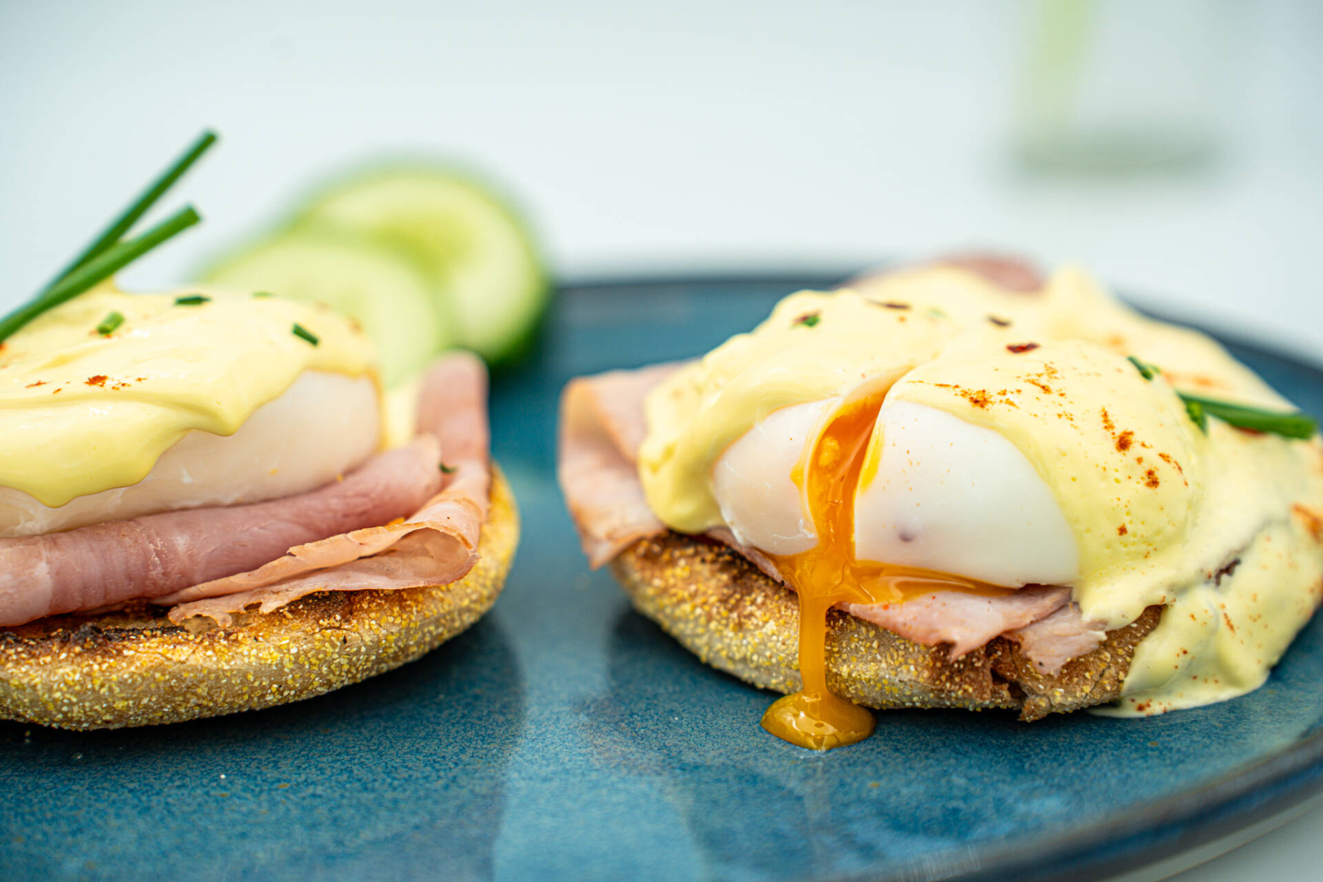 Zwei Eggs Benedict mit pochierten Eiern, Sauce Hollandaise und Schinken liegen auf gerösteten English Muffins mit Beilagen.