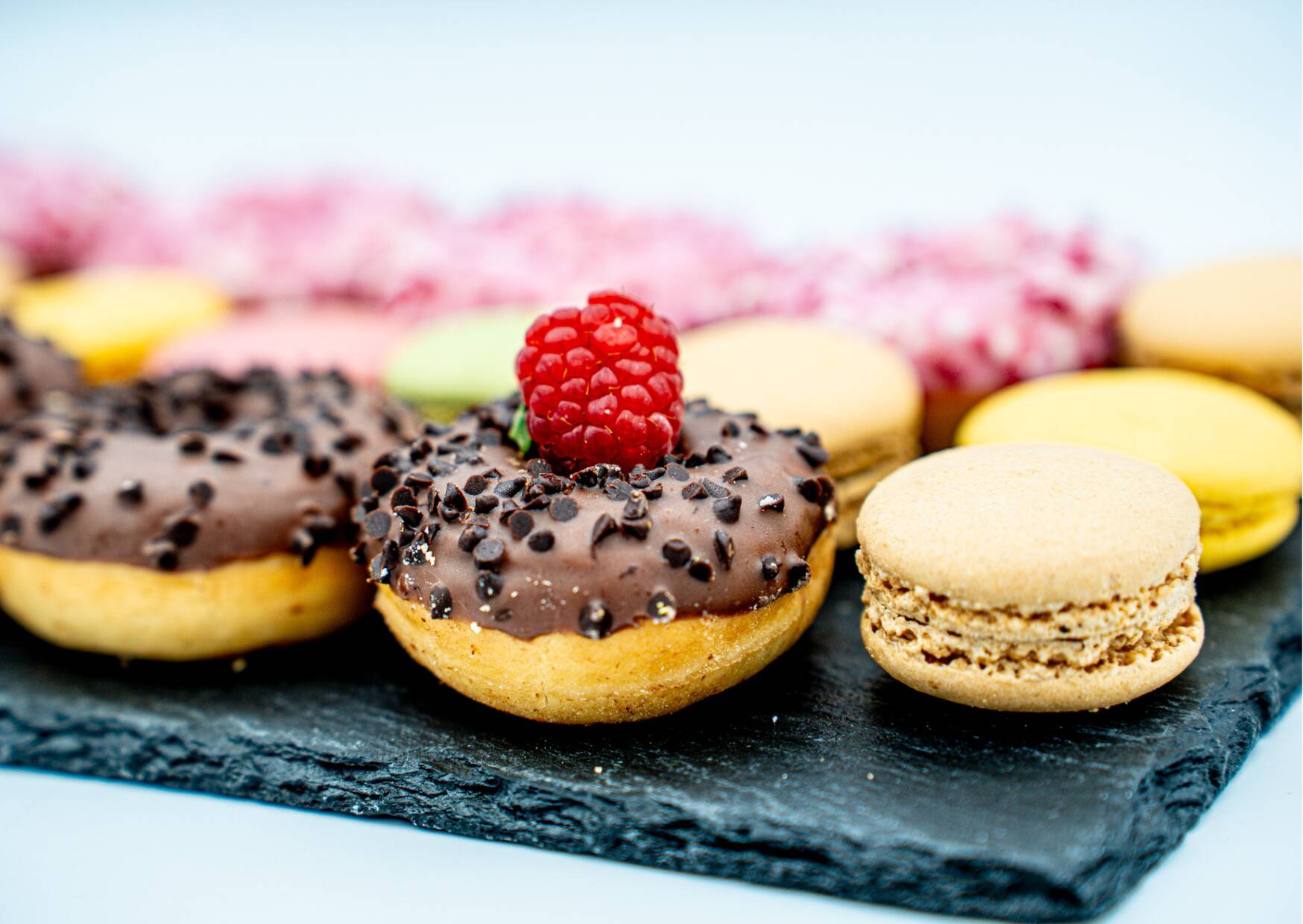 Various glazed pastries topped with chocolate pieces and a macaron lie on a black slate plate.