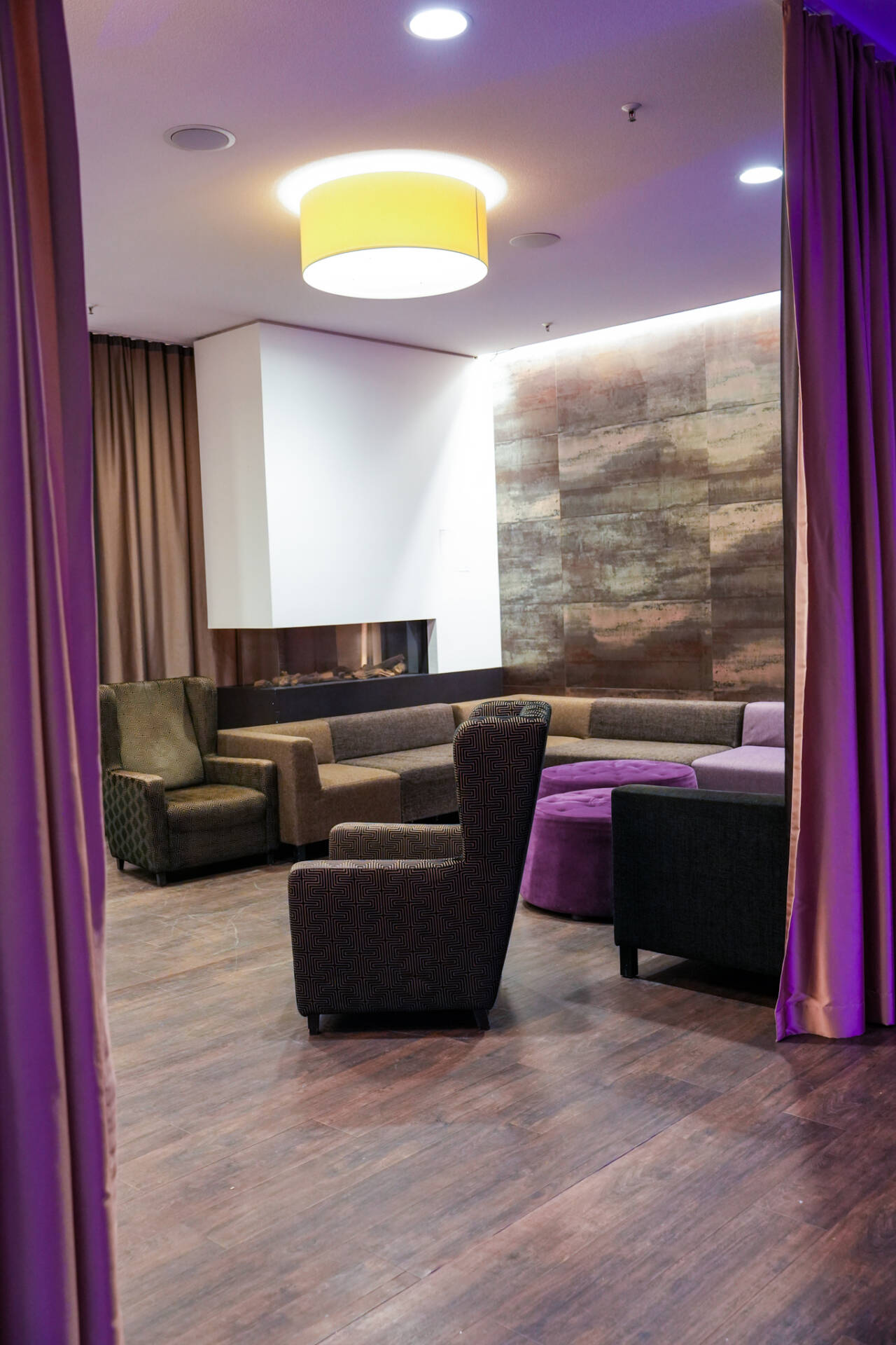 Eine gemütliche Sitzgruppe im Hotel mit Sesseln, Sofa, rundem Tisch, Holzfußboden, Vorhängen und dekorativer Wandgestaltung.