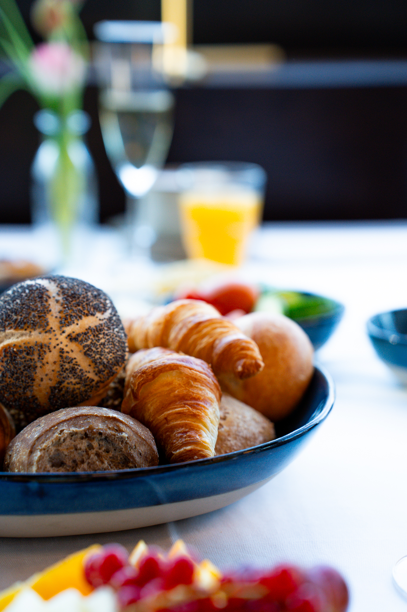 A breakfast plate with various rolls and croissants stands on a set table with drinks and fruit.