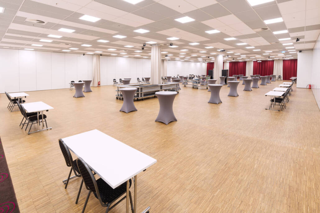 Eine große Eventhalle in Berlin Moabit mit Stehtischen, Bestuhlung, einem Holzfußboden und einer flexiblen Raumaufteilung für Konferenzen und Empfänge.