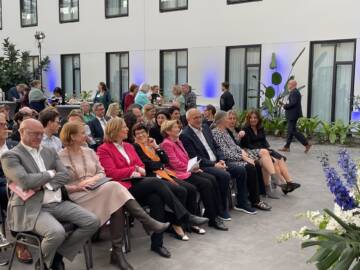 Mehrere Personen sitzen in einer Reihe auf Stühlen in einem Atrium mit weißen Wänden und blauen Lichtakzenten im Hotel MOA Berlin.