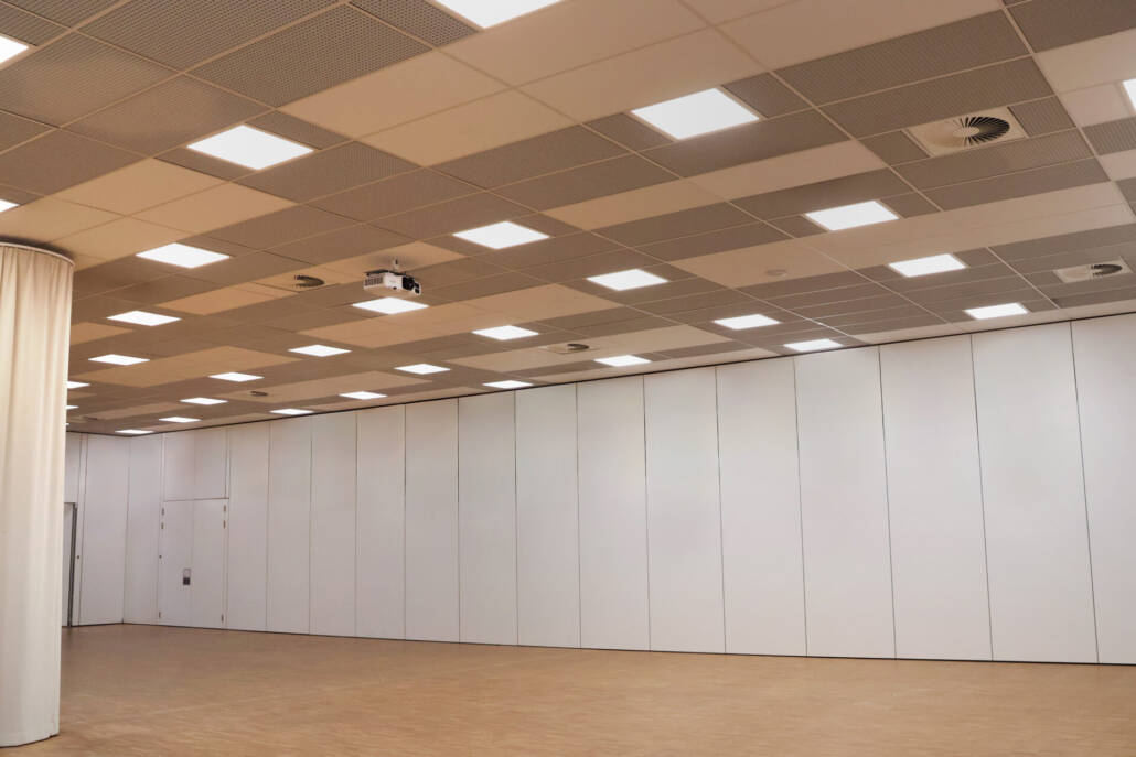Ein moderner, leerer Veranstaltungsraum mit modularen Trennwänden, einer integrierten Beleuchtung und Projektionsmöglichkeiten.