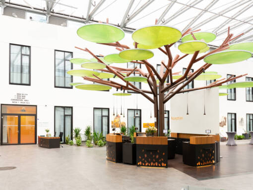 Ein offener Empfangsbereich in einem Berliner Coworking-Space mit einem modernen, baumförmigen Tresen und grünen, runden Deckenpaneelen.