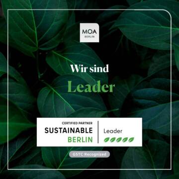 Ein grüner Blätterhintergrund mit Text 'Wir sind Leader' und dem Zertifikat 'Certified Partner Sustainable Berlin Leader' mit fünf Blattsymbolen - Eine Auszeichnung für das Hotel MOA Berlin in Mitte.