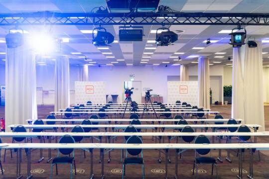 Ein großer, heller Konferenz- und Eventraum in Berlin Mitte mit Reihen von Tischen und Stühlen, zwei Kameras auf Stativen in der Mitte und Beleuchtung an der Decke.